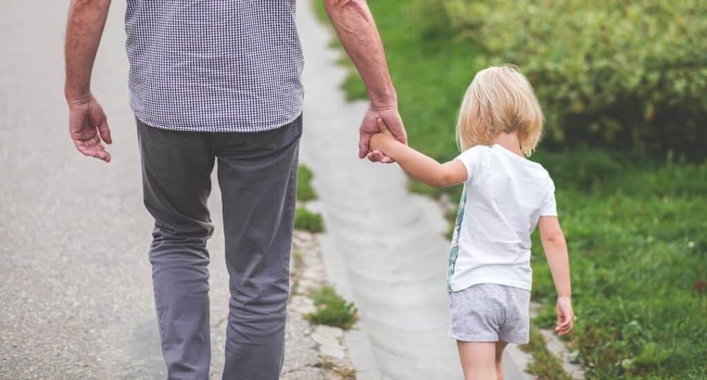 A parent holding a child's hand to illustrate satisfaction and happiness, one of the benefits of financial planning.